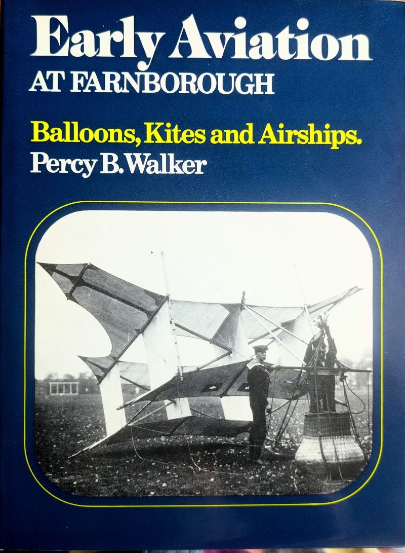 Picture of book cover showing 2 crew men on the ground preparing 'Cody' kite for flight with small circular wicker basket attached to carry one person.